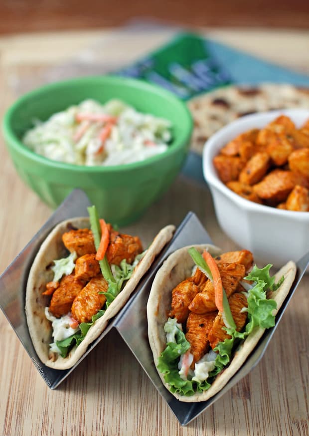Buffalo Chicken Tacos from Emily Bites shown in taco stand with slaw, chicken, and wraps in background