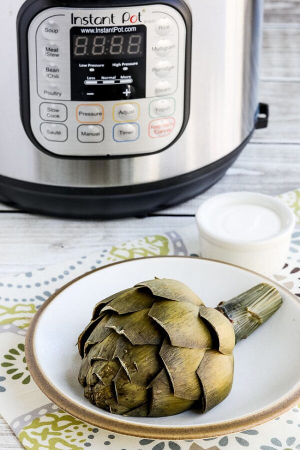 How to Cook Artichokes in the Instant Pot from Kalyn's Kitchen, photo with one artichoke half on plate in front and Instant Pot in back.