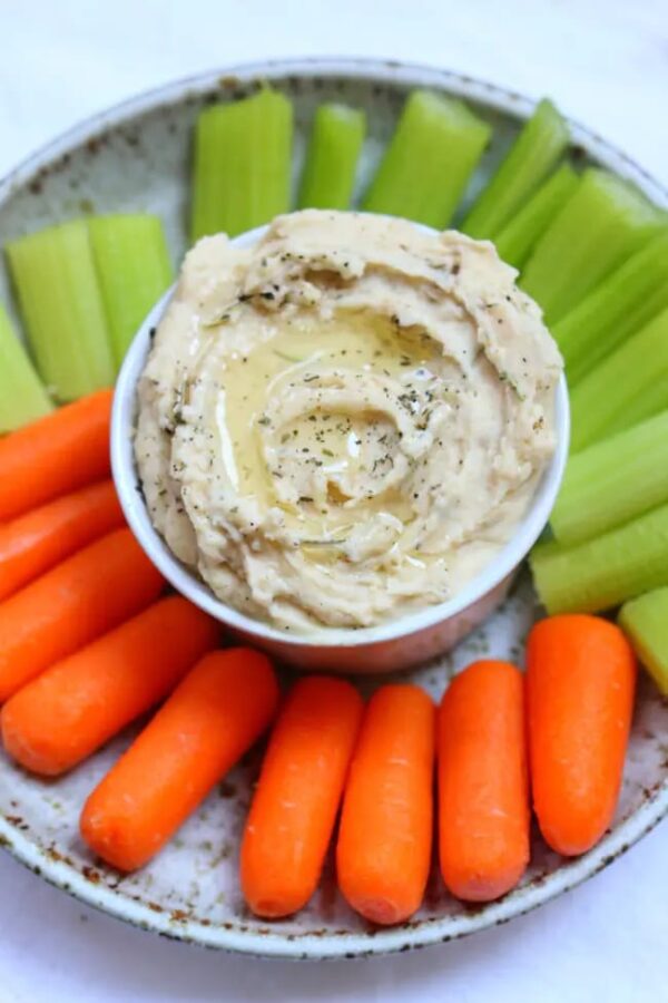 Instant Pot White Bean Garlic Hummus shown on plate with carrots and celery.