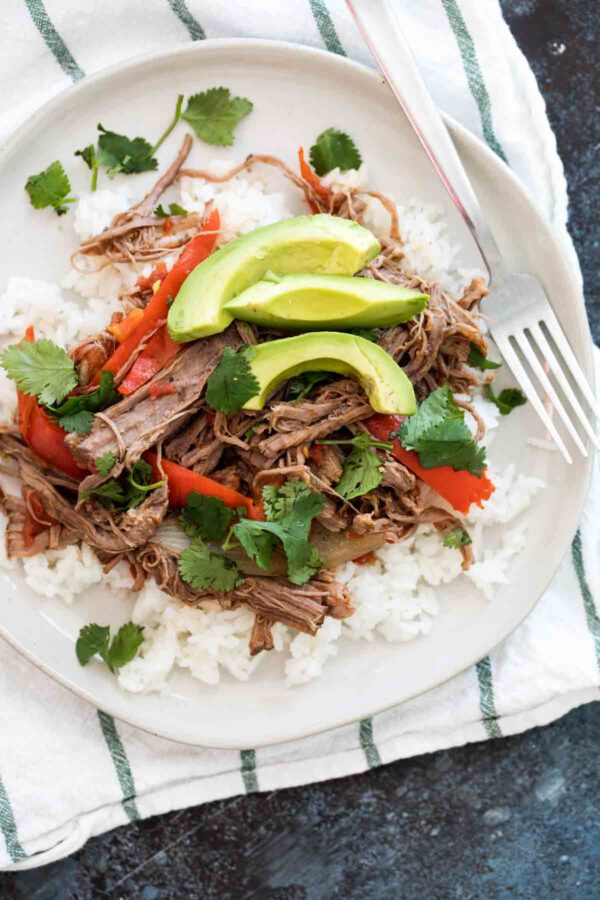 Slow Cooker Cuban Ropa Vieja from Taste and Tell shown on serving plate with peppers and avocado.