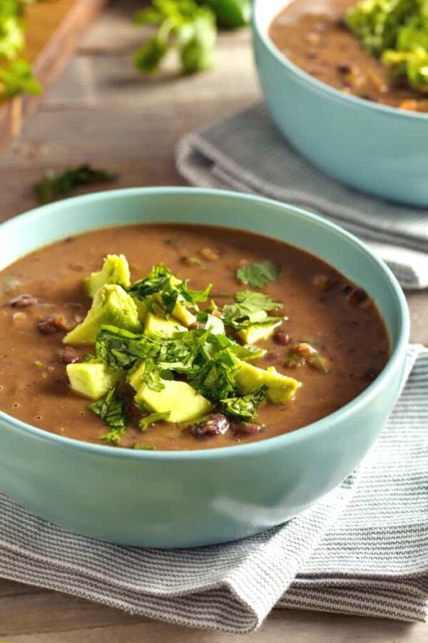 Four Ingredient Easy Slow Cooker Black Bean Soup shown in two bowls with avocado garnish.